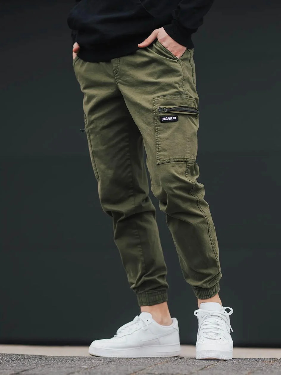 Chłopak ubrany w spodnie typu jogger cargo w kolorze oliwkowej od Jigga Wear. Joggery są materiałowe z pojemnymi kieszeniami bocznymi